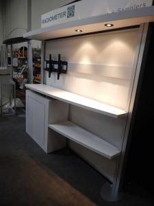 RENTAL: RE-1019 with White Laminated Sconce with Puck Lighting, RE-1201 Tapered Counter, White Laminated Backwall Counter & Shelves, Large Monitor Mount, 42" Monitor, RE-171 Literature Stand, Tension Fabric Panel for Backwall, Sintra Header Graphic, and V